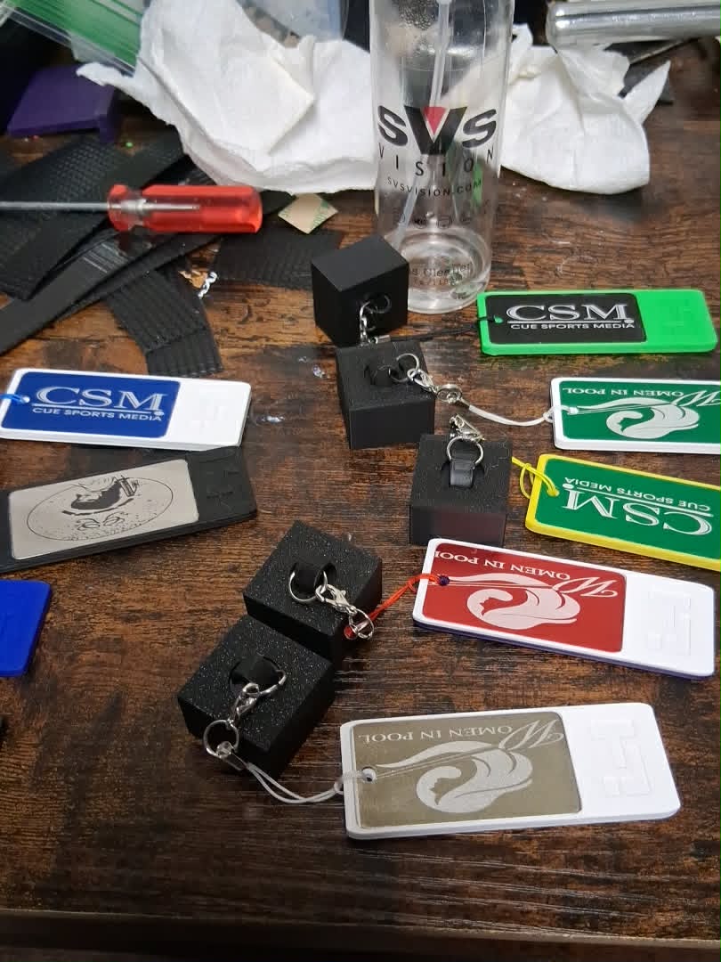 "Custom Chalk Holder black 3D-printed pool chalk keychains with clip — shown alongside custom branded keychains for CSM Cue Sports Media and Women in Pool in multiple colors"